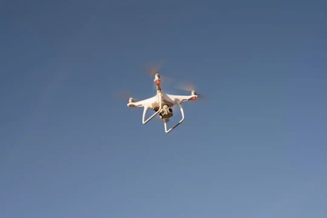 Drone putih terbang di langit biru cerah, melambangkan teknologi modern.