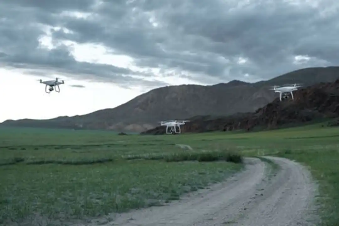 Drone melayang di atas lanskap indah dengan ladang dan pegunungan di bawah langit mendung
