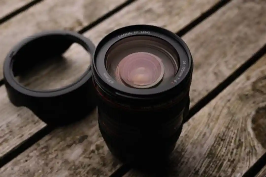 Close-up lensa Canon EF dengan hood di atas meja kayu bertekstur, cocok untuk tema fotografi dan pelatihan.