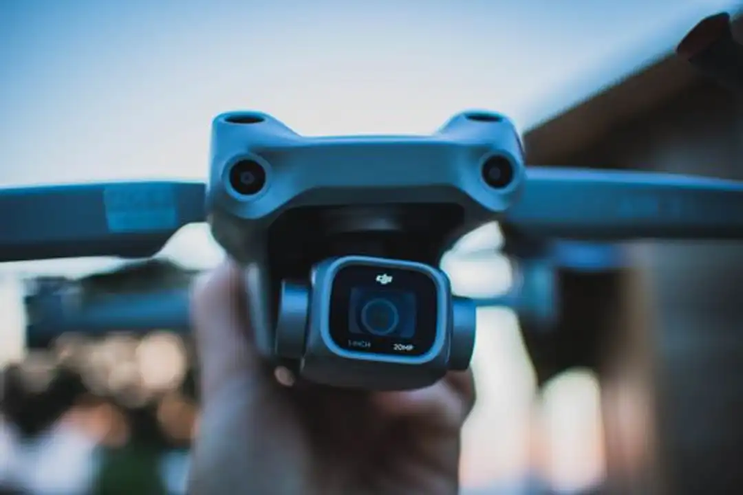 Tangan memegang kamera drone, close-up detail, latar belakang buram, outdoor.